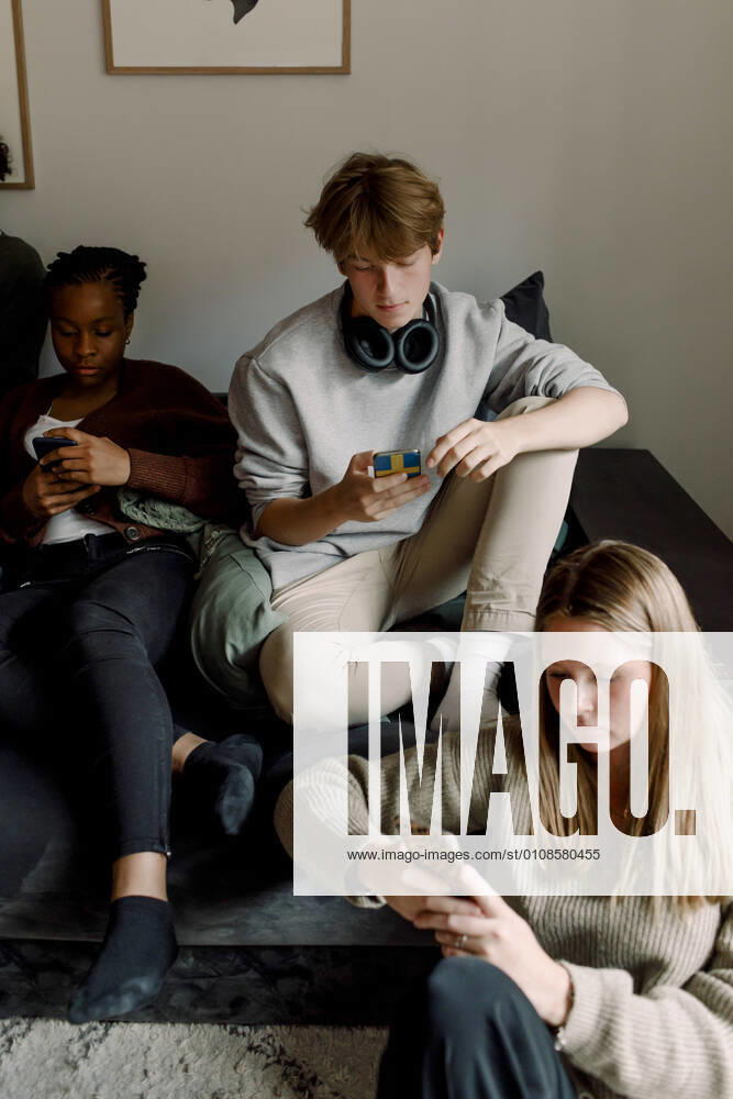 Teenage girls and boy using mobile phone while sitting in living room Sweden, Stockholm, model released, property released