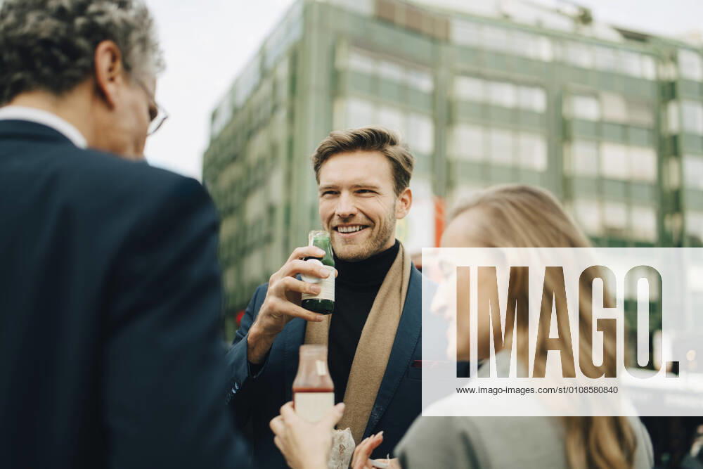 IMAGO Creative: Corporate: Klimaschutz, Digitalisierung und Urbanisierung Smiling male entrepreneur with drink looking at coworkers in city Germany, Hamburg, model released