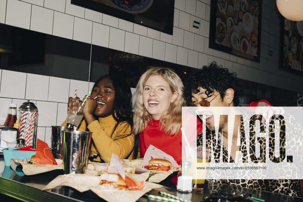 Portrait of happy woman with friends eating burger during social gathering at cafe Sweden, Stockholm, model released, property released