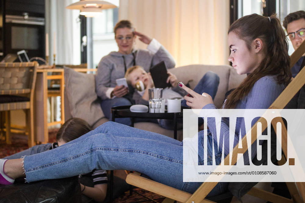 IMAGO Creative: Jahreszeit Winter, Couching Teenage girl using smart phone while relaxing with family in living room at home Sweden, Stockholm, model released, property released
