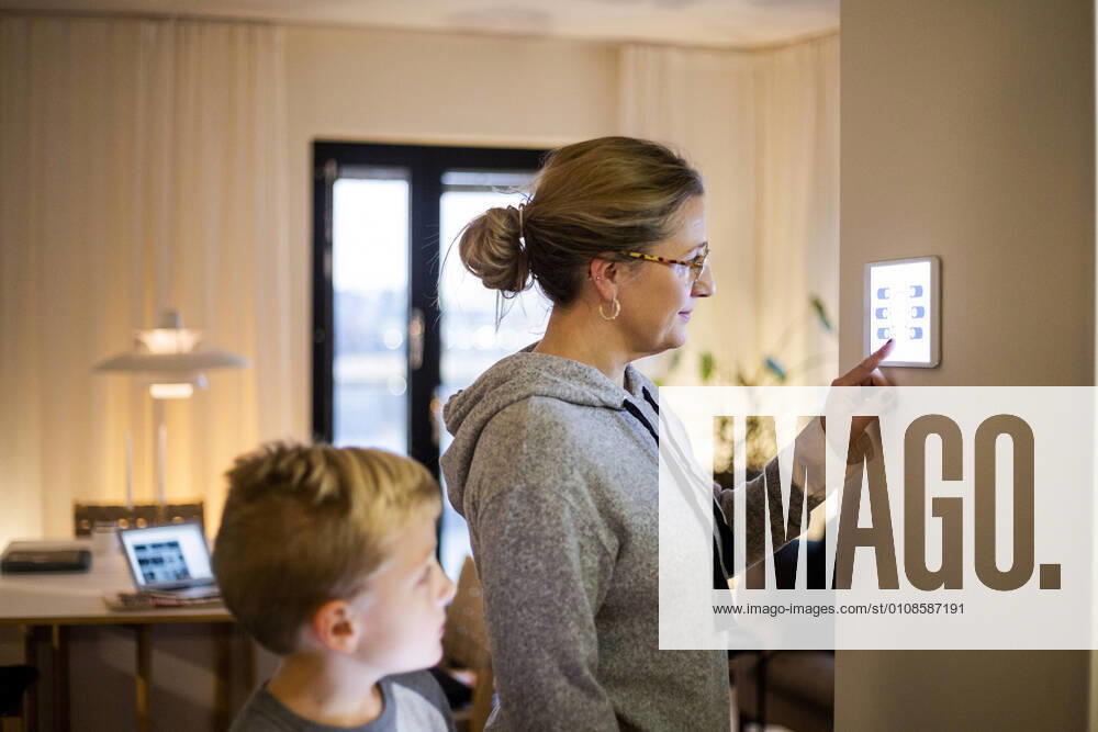 IMAGO Creative: Corporate: Klimaschutz, Digitalisierung und Urbanisierung Son looking at mother using digital tablet mounted on wall at smart home Sweden, Stockholm, model released, property released
