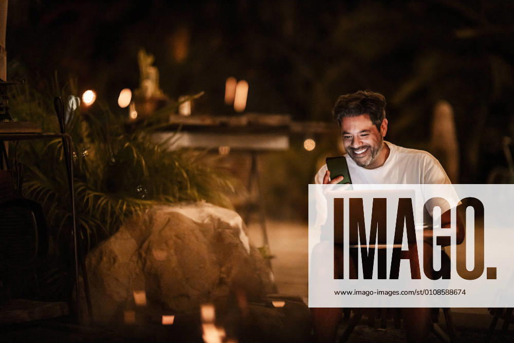 Happy man using phone and laptop at night USA, California, model released
