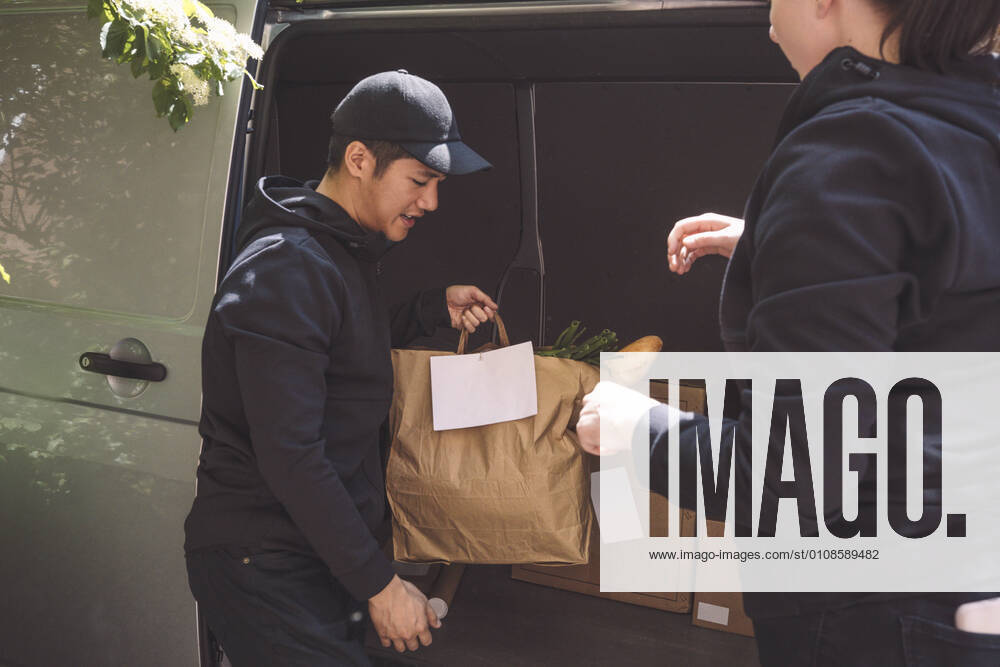 Delivery man talking to female colleague while holding package near truck Sweden, Stockholm, model released