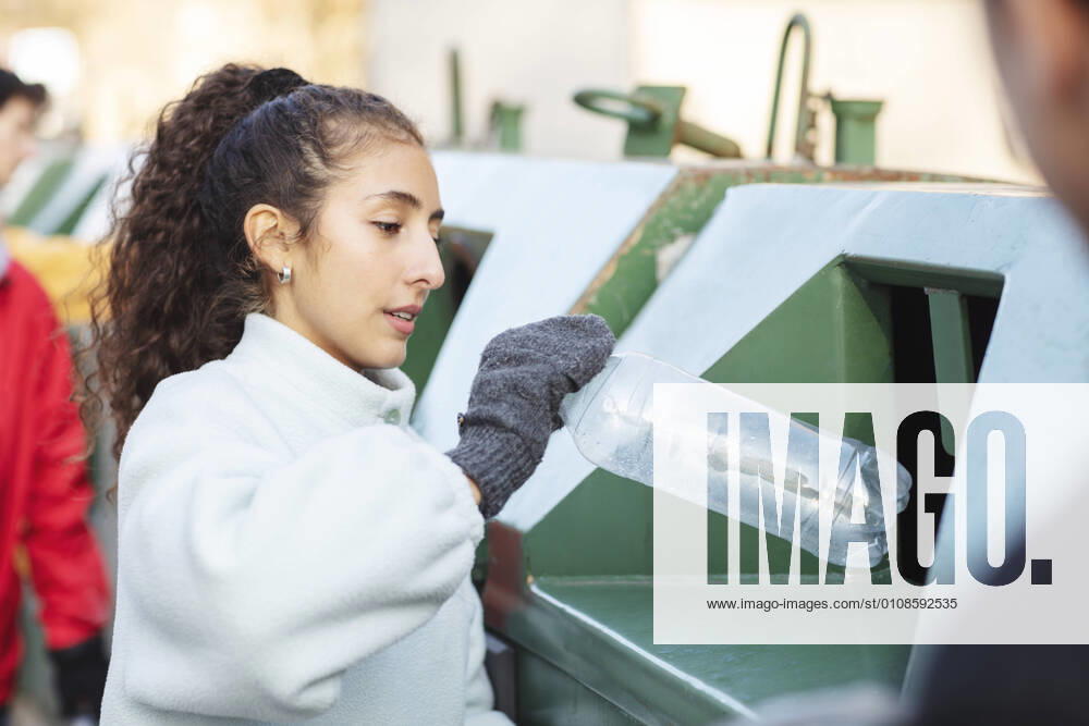 IMAGO Creative: Klimawandel - Umwelterziehung Smiling female environmentalist with friend throwing plastic bottle in garbage can Sweden, Stockholm, model released