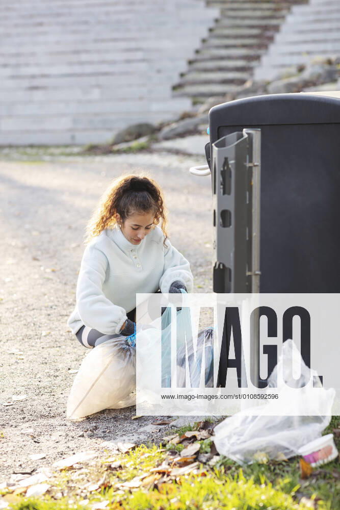 IMAGO Creative: Klimawandel - Umwelterziehung Female volunteer crouching with plastic waste by garbage can Sweden, Stockholm, model released