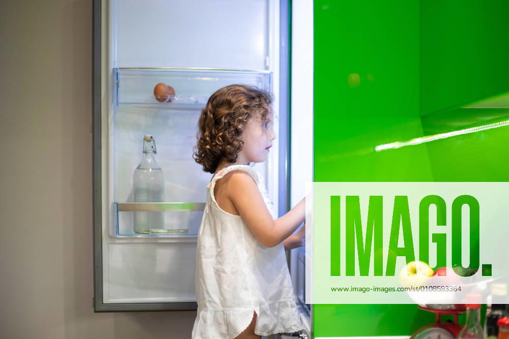 IMAGO Creative: Gesellschaft, Armut Little girl in sleepwear searching for snack inside open refrigerator at night in kitchen at home