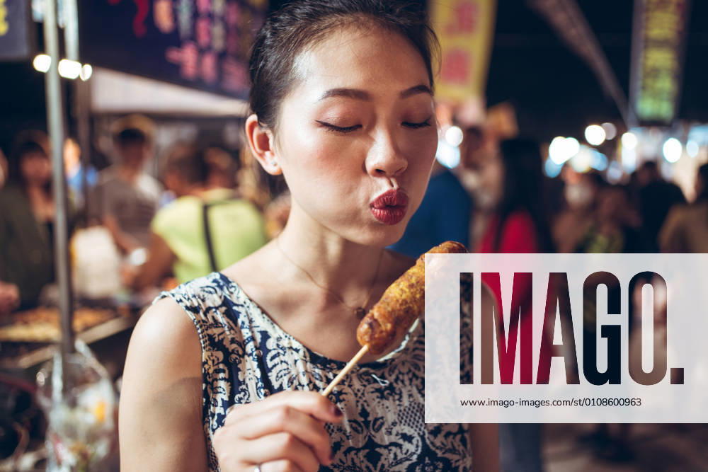Asian female standing in Zhubei Night Market and cooling hot sausage on stick