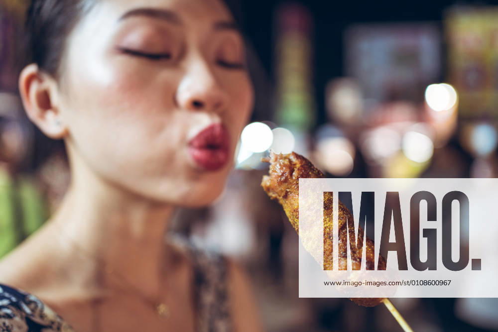 Asian female standing in Zhubei Night Market and cooling hot sausage on stick