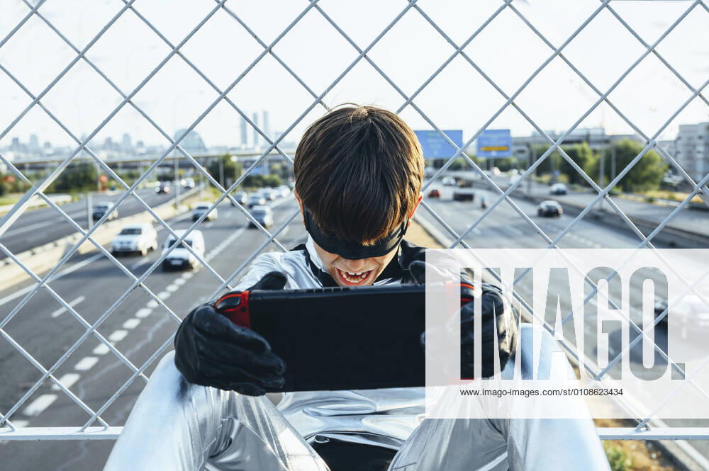 Screaming boy disguised as superhero using games cosole above the streets of the city model released Symbolfoto JCMF00213
