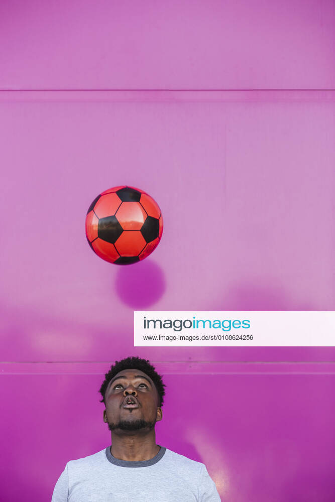 Young man juggling with soccer ball against pink wall in city model released Symbolfoto LJF01679