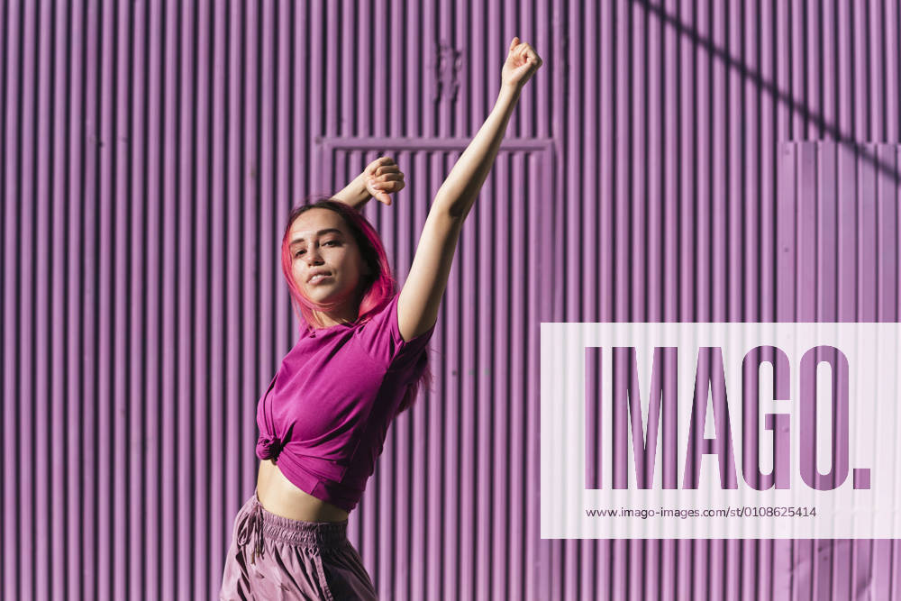 Young woman with dyed red hair dancing in front of purple wall in the city model released Symbolfoto TCEF00999