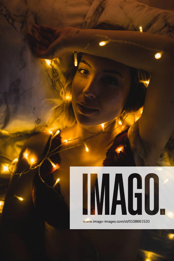 From above young beautiful woman in underwear lying in bed surrounded by light garland, Model released