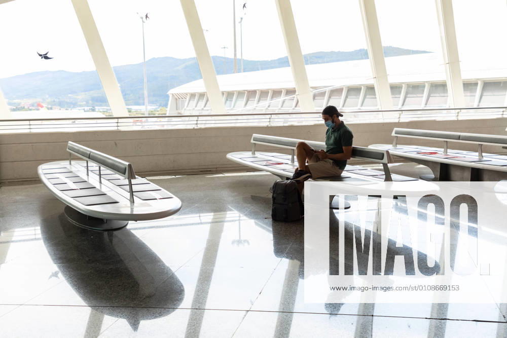 IMAGO Creative: 2021 Trends Side view of male tourist in protective mask sitting in departure lounge of airport and speaking on mobile phone while waiting for flight during coronavirus pandemic