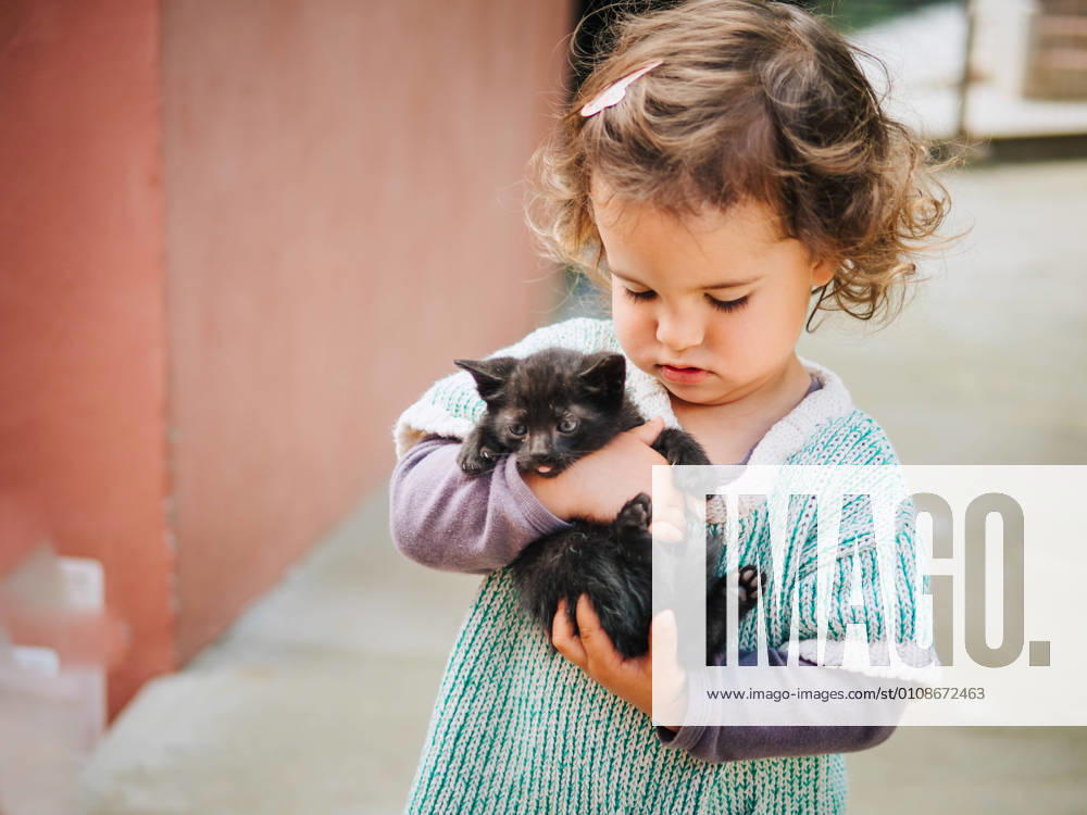 Tender scene of cute little girl holding and rocking a small black pussycat