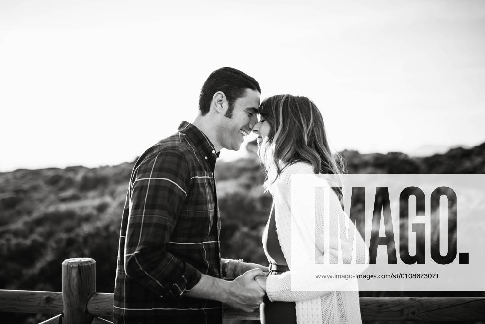 Handsome adult male smiling and kissing beautiful pregnant female from back while standing on sandy beach together, Model released