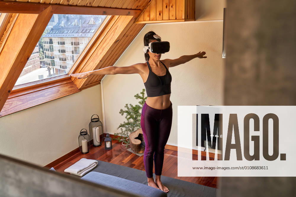 IMAGO Creative: Sport Start-Up Full body barefoot lady in VR glasses standing in Mountain pose with clasped hands while doing yoga in morning at home
