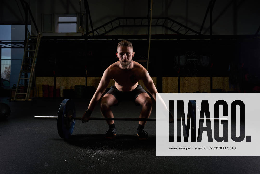 Strong man with barbell with weights in his hands doing strength exercises in the gym with magnesium in his hands. Young athlete practicing multidisciplinary training