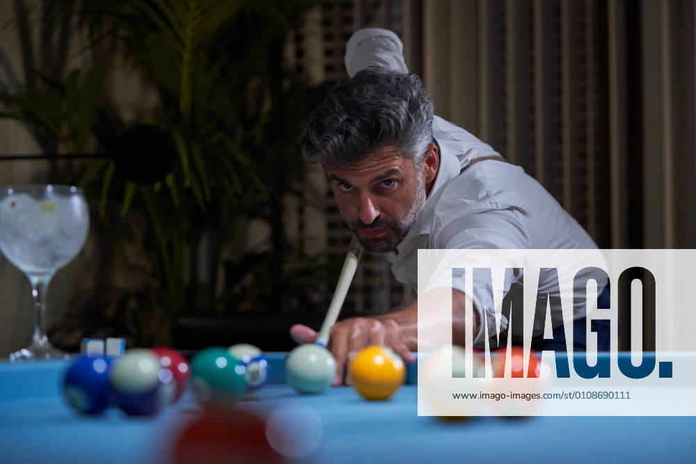 Confident focused gray haired male in white shirt preparing for shot with cue while playing billiards game