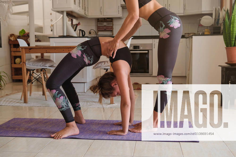 Mother and daughter wearing the same sport clothes practicing yoga acrobatics at the kitchen of a house together, Model released, Property released