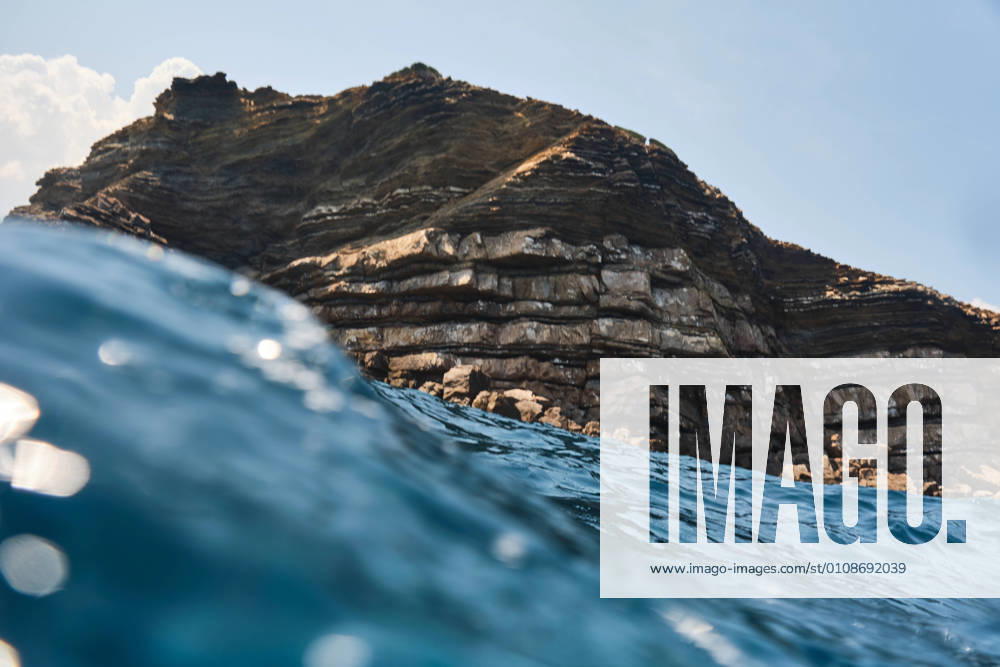 IMAGO Creative, Jahreszeit Sommer, Sommerferien Sea wave glistens in sunlight in front of high rocky cliff on sunny summer day