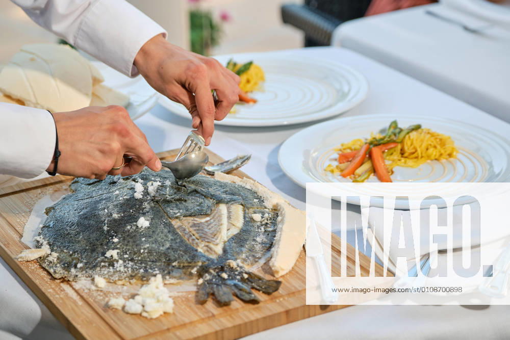 Closeup of yummy juicy aromatic fish baked in salt dough crust being served by anonymous chef in restaurant, Model released, Property released