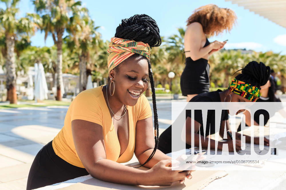 IMAGO Creative, Mainstream-Aktivismus IMAGO Creative: Frauenmonat, Feministischer Aktivismus Serious ethnic female with afro hairstyle creating cardboard poster with black lives matter inscription next to another black woman texting on phone during demonstration, Model released