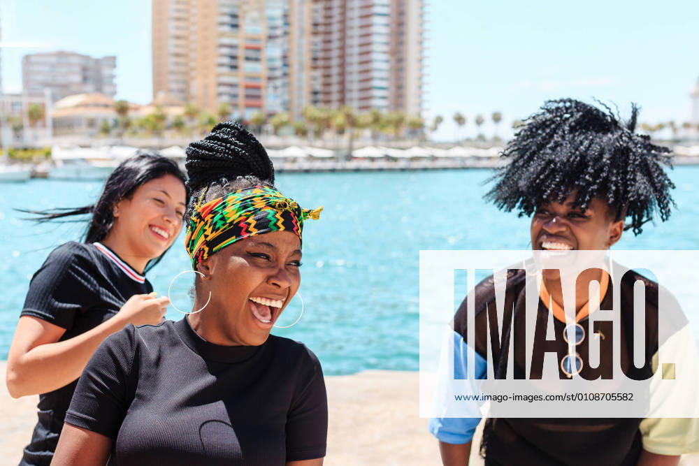 IMAGO Creative, Jahreszeit Sommer, Sommer in der Stadt IMAGO Creative: Urban Diversity Company of diverse female friends laughing during city stroll near waterside in summer, Model released