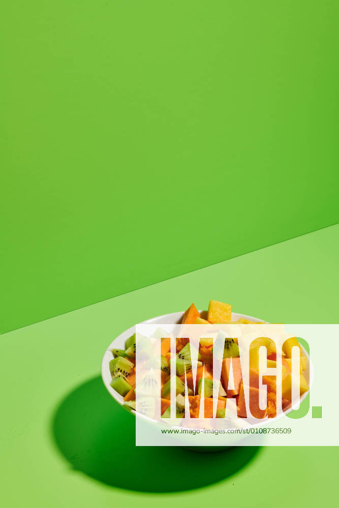 Closeup of delicious healthy natural fruit salad with chopped papaya and kiwi served in plate placed on bright green background