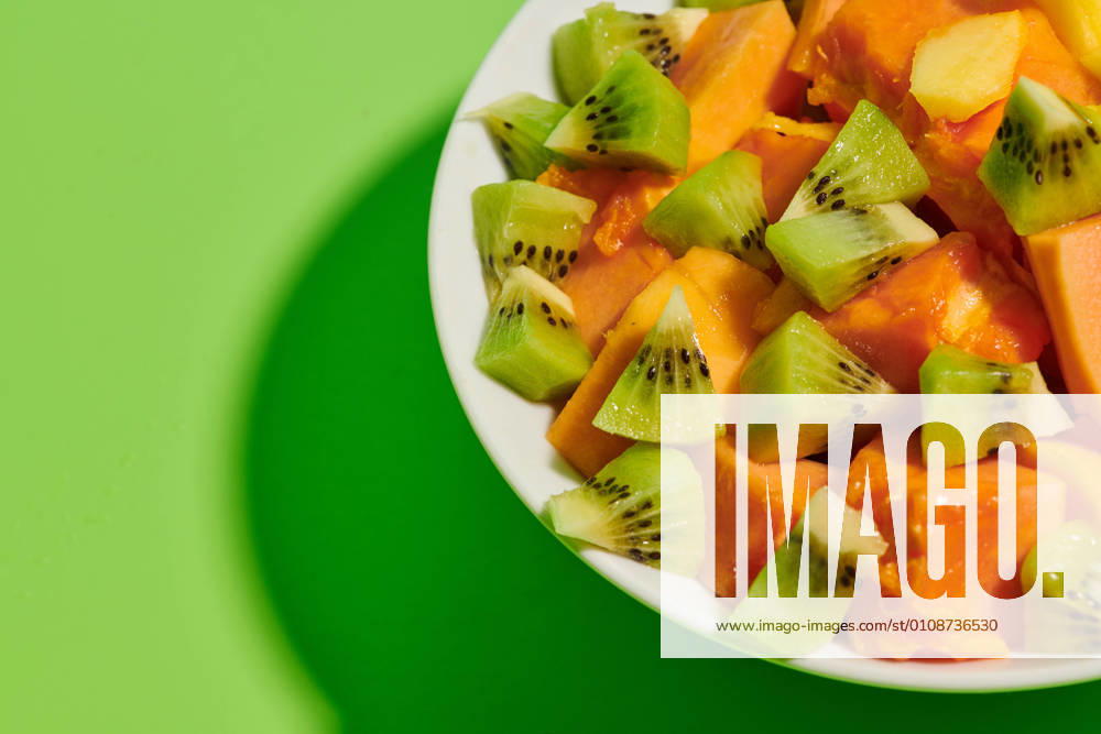 Closeup of delicious healthy natural fruit salad with chopped papaya and kiwi served in plate placed on bright green background