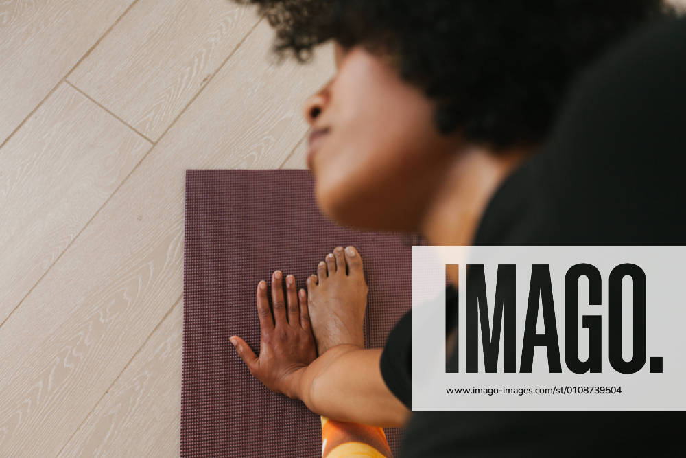 From above close-up view of African American attractive young woman performing yoga pose with closed eyes on a mat at home, Model released