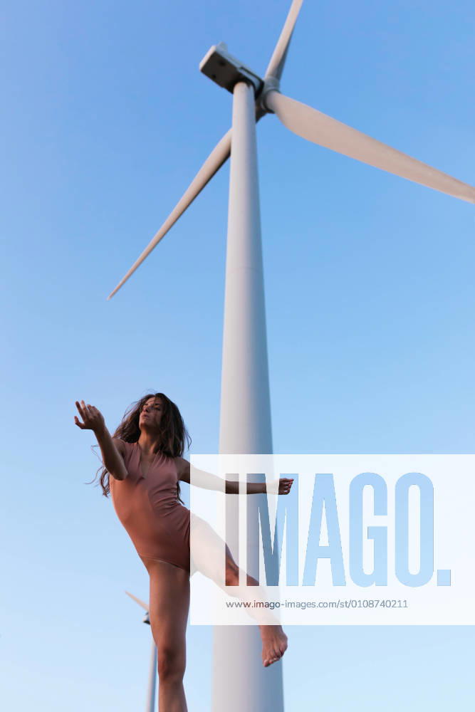 IMAGO Creative: N?chste Generation, Sozial- und klimabewusst Young slim lady dancing under windmill on sunny day