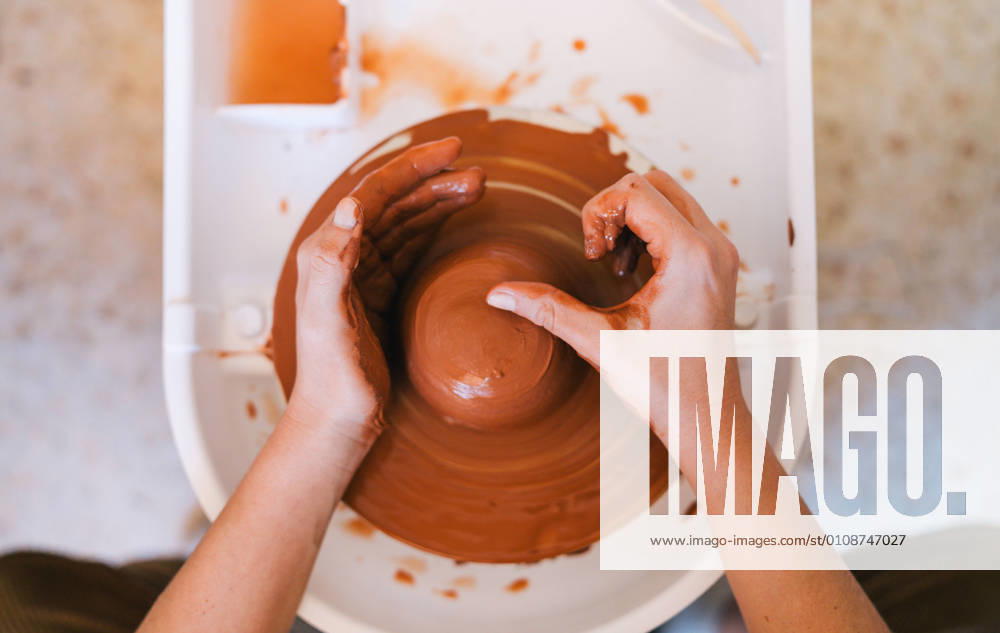 High angle of crop person in casual clothes making handmade pottery using special equipment while working in light contemporary studio