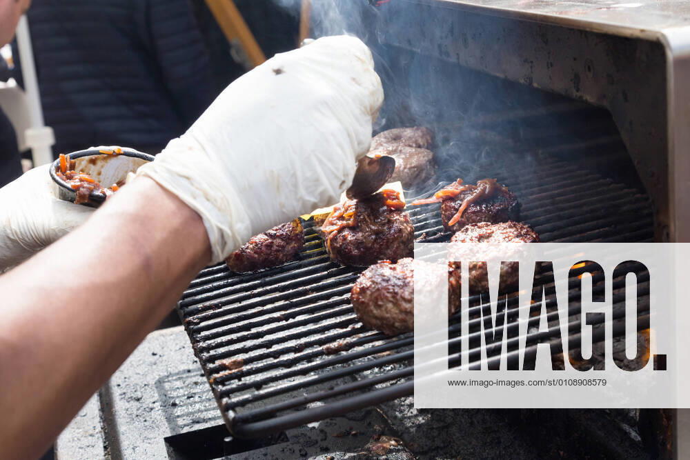Beef burgers being grilled on food stall grill. Chef making beef burgers outdoor on open kitchen international food festival event. Street food ready to serve on a food stall.burger, grill, hamburger, street food, food, beef, stall, street, fast, meat, snack, outdoors, cuisine, seller, vendor, catering, lunch, meal, delicious, restaurant, junk food, sauce, outdoor, urban, event, making, chef, decorate, to go, take out, cart, plate, dressing, healthy, city, open kitchen, cheese, bacon, specialty, topping, pork, oven, stove, glove, fest,