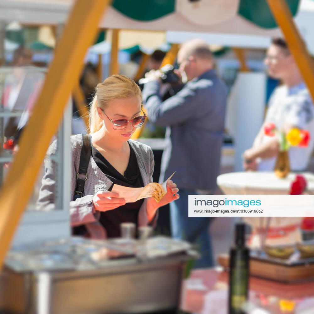 Woman buying meal at street food festival. Beautiful blonde caucasian lady buying freshly prepared meal at a local street food festival. Urban international kitchen event in Ljubljana, Slovenia, in summertime., model releasedwoman, food, market, grill, barbecue, street, people, young, shop, beautiful, healthy, outdoors, festival, fresh, lady, customer, urban, female, city, face, drink, stall, european, buy, vegetable, person, lifestyle, produce, attractive, summer, beverage, purchase, organic, portrait, marketplace, tourism, tourist, event, market stall, market stand, leisure, buying, stand, juise, sunglasses, cook, hat, casual, crowd, look,