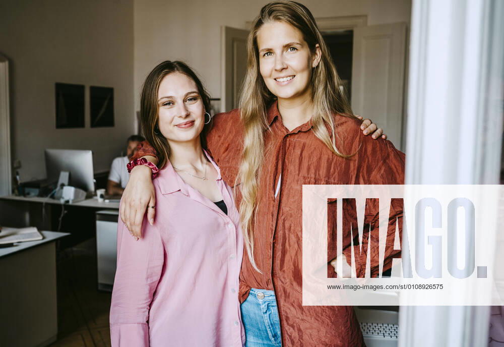 Smiling female colleagues with arms around standing in office Germany, Berlin, model released, property released