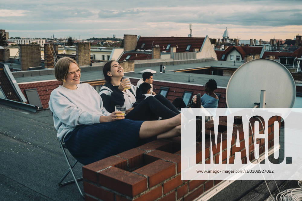 IMAGO Creative, Lifestyle, Leben in einer Wohngemeinschaft, WG IMAGO Kreativ: Urbane Kultur - Sommer auf den Dächern Smiling female talking to friend while enjoying drink on building terrace Germany, Berlin, model released, property released
