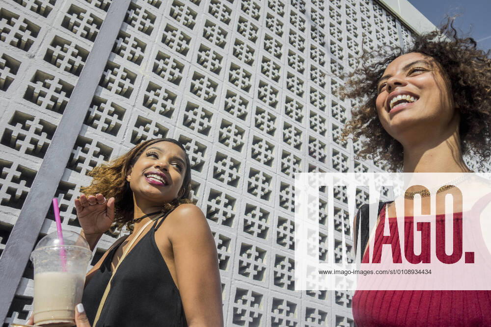Cheerful young female friends walking by wall on sunny day model released Symbolfoto AJOF00616