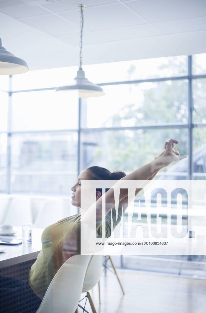 Tired young businesswoman stretching arms while sitting at desk in office model released Symbolfoto property released AJOF00737