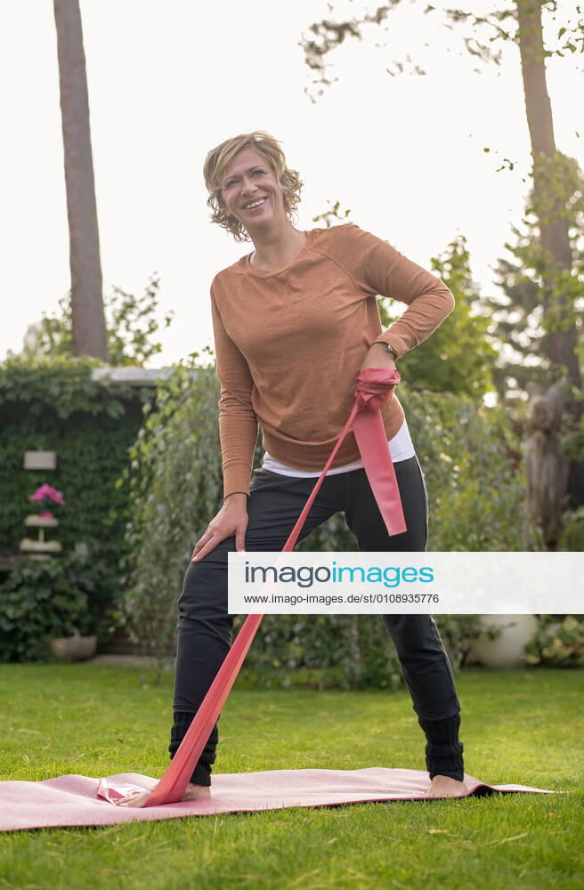 Smiling woman exercising with resistance band while standing at back yard model released Symbolfoto property released BFRF02315
