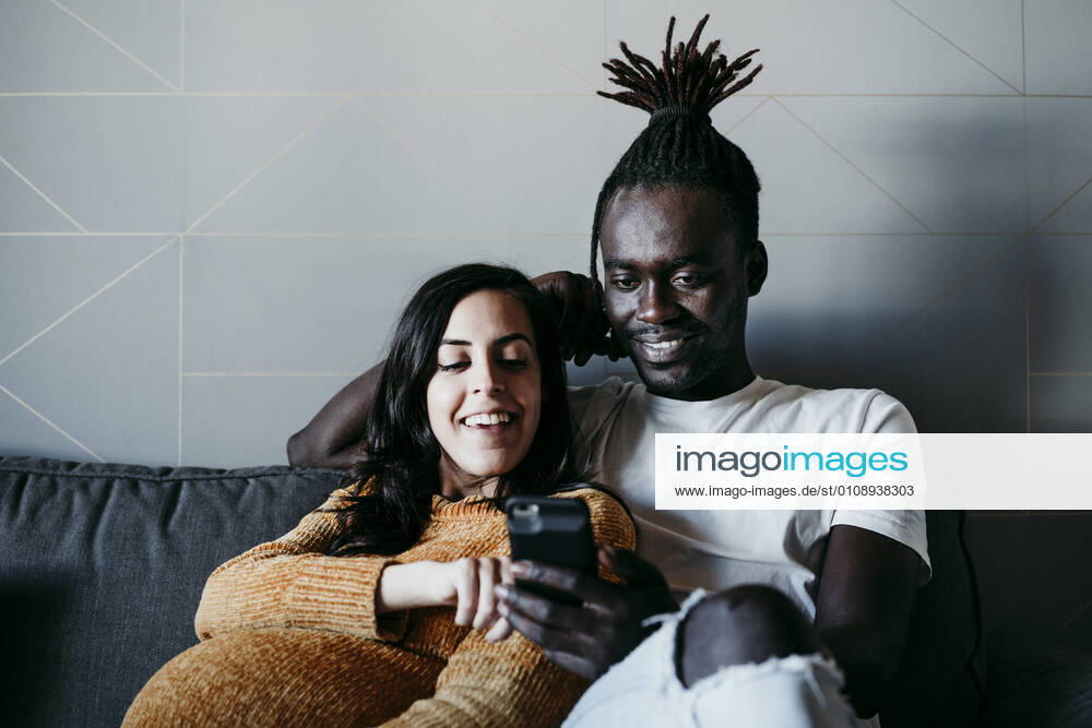 Smiling young man and pregnant woman using mobile phone in living room at home model released Symbolfoto property released EBBF01594