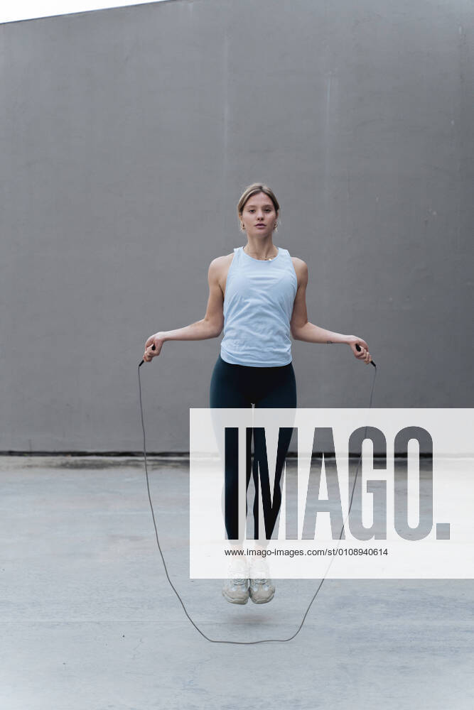 Young woman skipping rope while standing against wall model released Symbolfoto FMOF01261