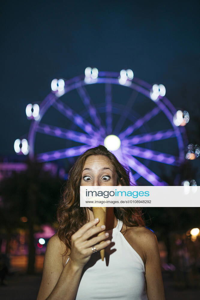 Woman looking at ice cream while standing against ferries wheel in city model released Symbolfoto MTBF00744