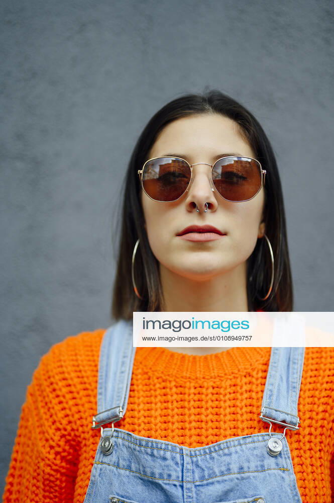 Young woman wearing sunglasses standing against gray wall model released Symbolfoto PGF00220
