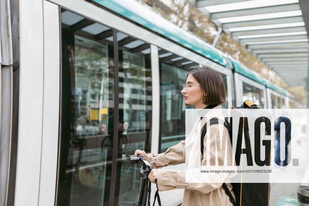 Woman with instrument case and electric push scooter standing by tram in city model released Symbolfoto VABF03969