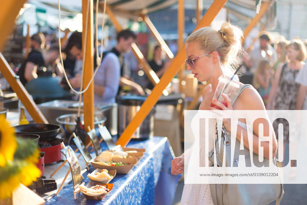 Woman buying meal at street food festival. Beautiful blonde caucasian lady wearing white summer dress buying freshly prepared meal at a local street food festival. Urban international kitchen event in Ljubljana, Slovenia, in summertime., model releasedwoman, food, market, grill, barbecue, street, people, young, shop, beautiful, healthy, outdoors, festival, fresh, lady, customer, urban, female, city, face, drink, stall, european, buy, vegetable, person, lifestyle, produce, attractive, summer, beverage, purchase, organic, portrait, marketplace, tourism, tourist, event, market stall, market stand, leisure, buying, stand, juise, sunglasses, cook, hat, casual, crowd, look,