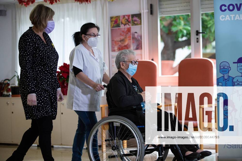 Josefa PÃ rez, 89 years old, accompanied by a health worker, is the first woman to be vaccinated in Catalonia, during the first day of vaccination in Spain, in the Feixa Llarga retirement home in L Hospitalet de Llobregat, in Barcelona (Spain), on 27 December 2020. The first doses of the vaccine developed by Pfizer and BioNtech laboratories arrived in Spain yesterday, December 26, at a Pfizer warehouse in Guadalajara by land from Puurs (Belgium). Starting Monday, weekly deliveries will be made to the autonomous communities with an average of 350,000 doses prioritized for four population groups: residents and health and social-health personnel in homes for the elderly and disabled; front-line health personnel; other health and social-health