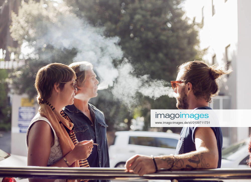 Friends smoking while standing outdoors on sunny day model released Symbolfoto AJOF00383