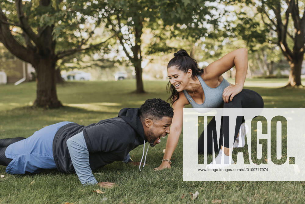 Smiling woman looking at man doing push up at backyard model released Symbolfoto SMSF00408