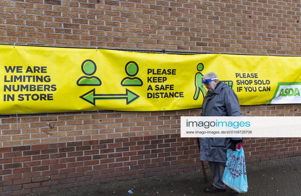 A man wearing a face mask walks past a Covid19 awareness sign outside ASDA supermarket in Wales. Newport United Kingdom - ZUMAs197 20210111_zab_s197_018