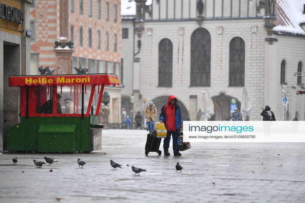 Theme picture Winter in the Coronavirus Pandemic Prolongation Lockdown until 31 January 2021 Empty streets and squares Only a few passers-by go over the Marienplatz in Munich on 12 01 2021 A homeless man walks with his belongings past a hot chestnut stand in the foreground cavorting pigeons people, passers-by